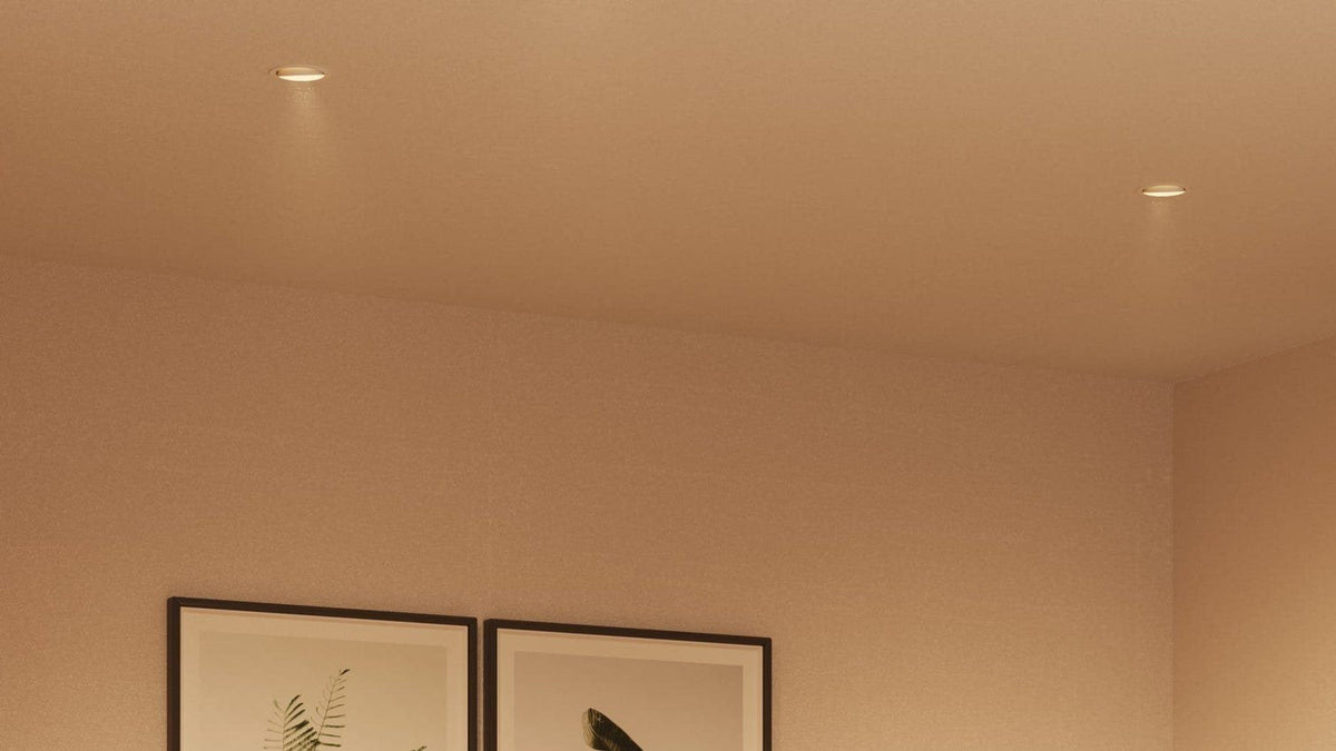 Two recessed downlights lit in the ceiling of a warm living room above framed botanical art