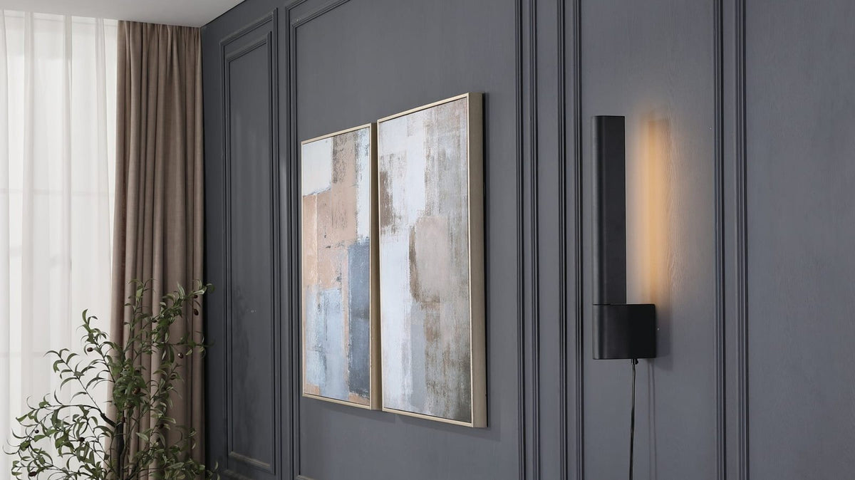 Black linear wall sconce lit on a dark paneled living room wall beside framed artwork
