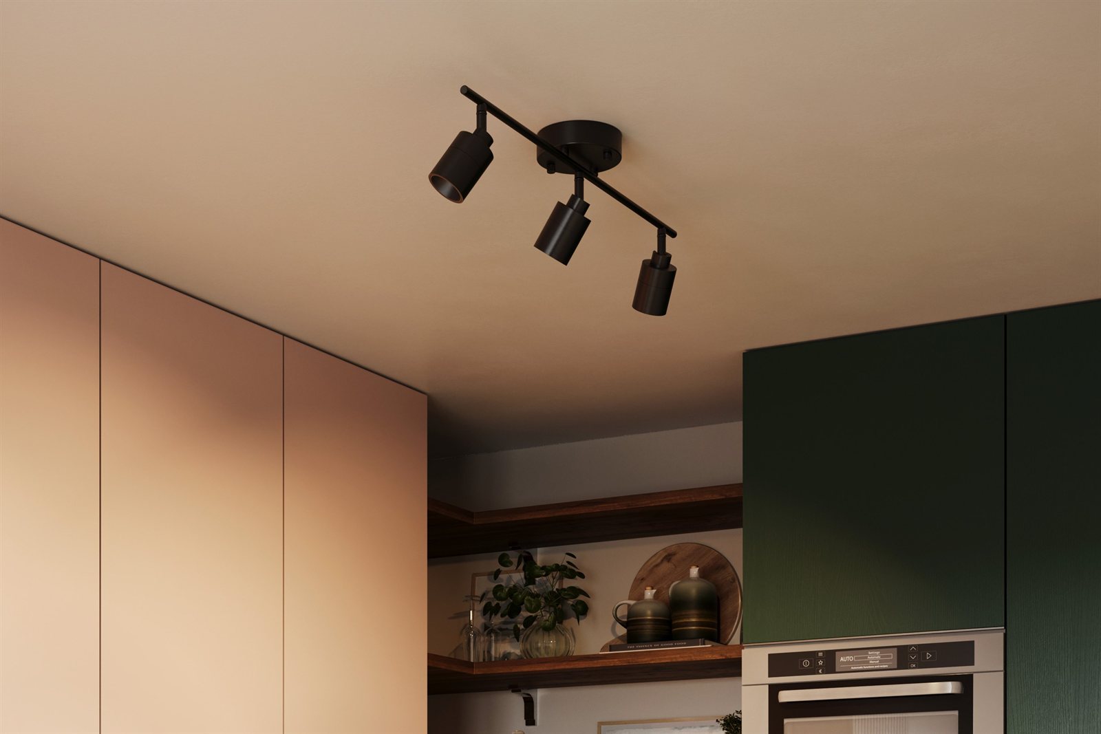 A dark Shura track light on the ceiling of a modern kitchen with blush and deep-green cabinetry